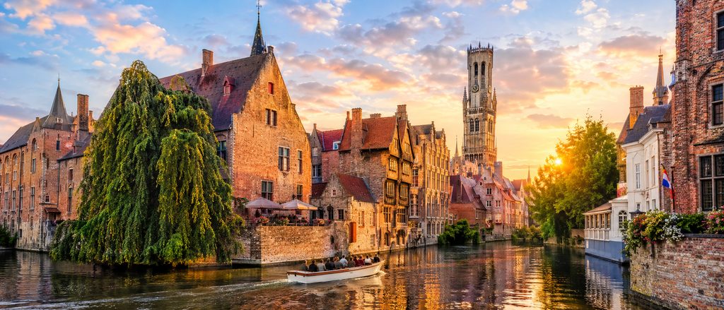 A canal and stepped gables in Bruges with Ghent's towers beyond